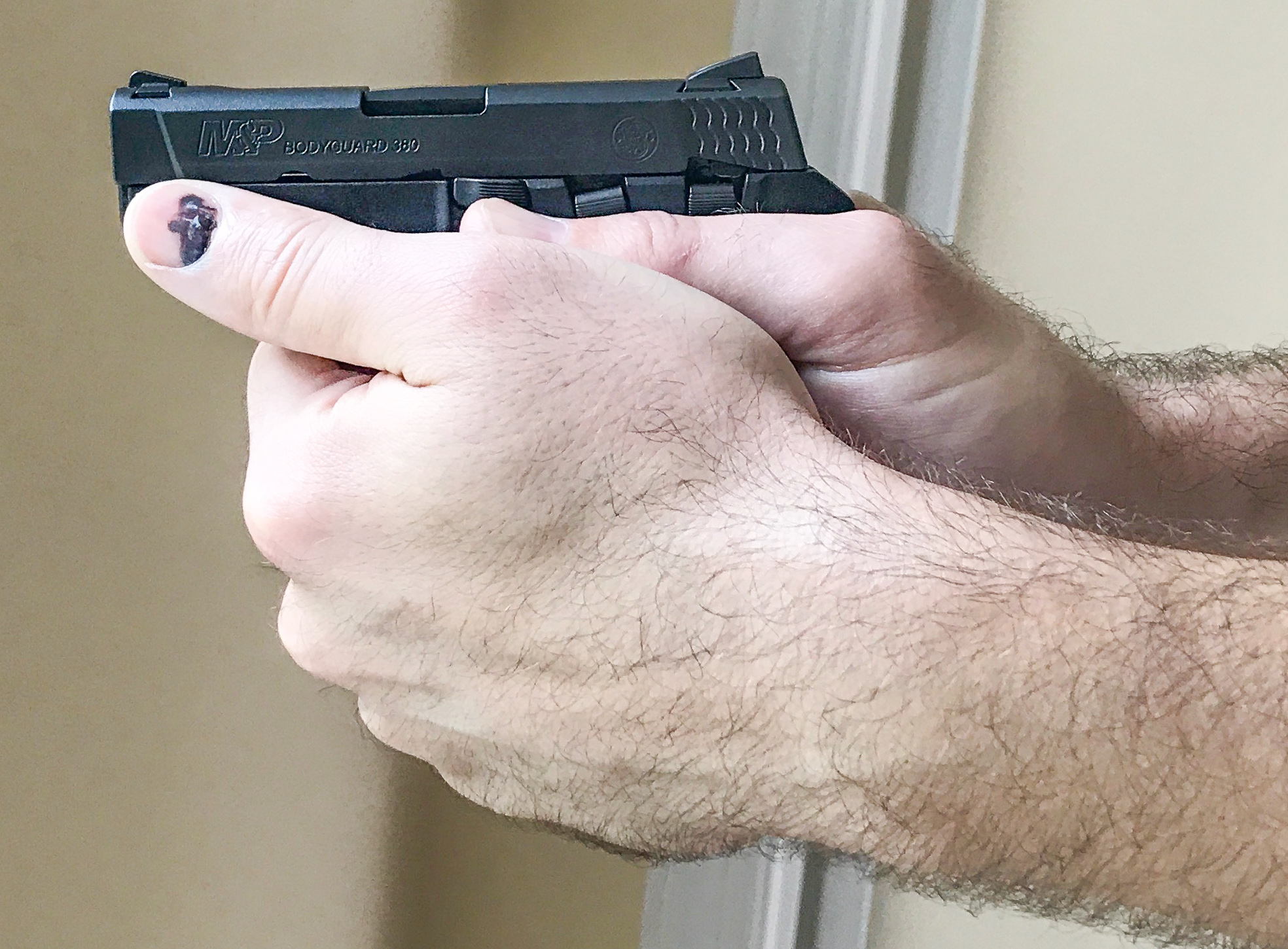 Support side view of two-handed grip on small pistol by large right-handed shooter